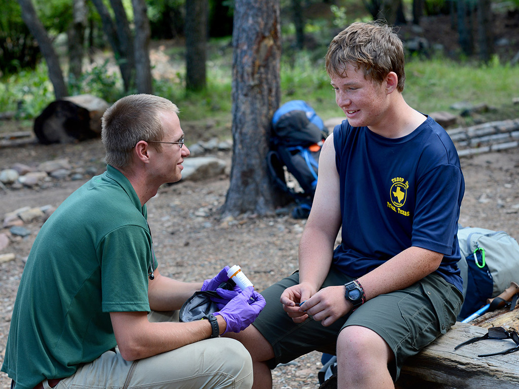 student kneeling down speaking to a young person out in the woods with a prescription in his hands